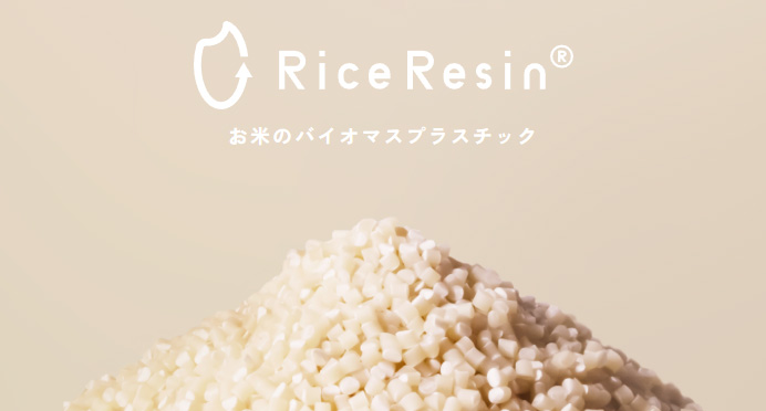 RiceResinのロゴと『お米のバイオマスプラスチック』という文字。ベージュの背景に、米粒のような白い樹脂ペレットが山状に積まれている。
